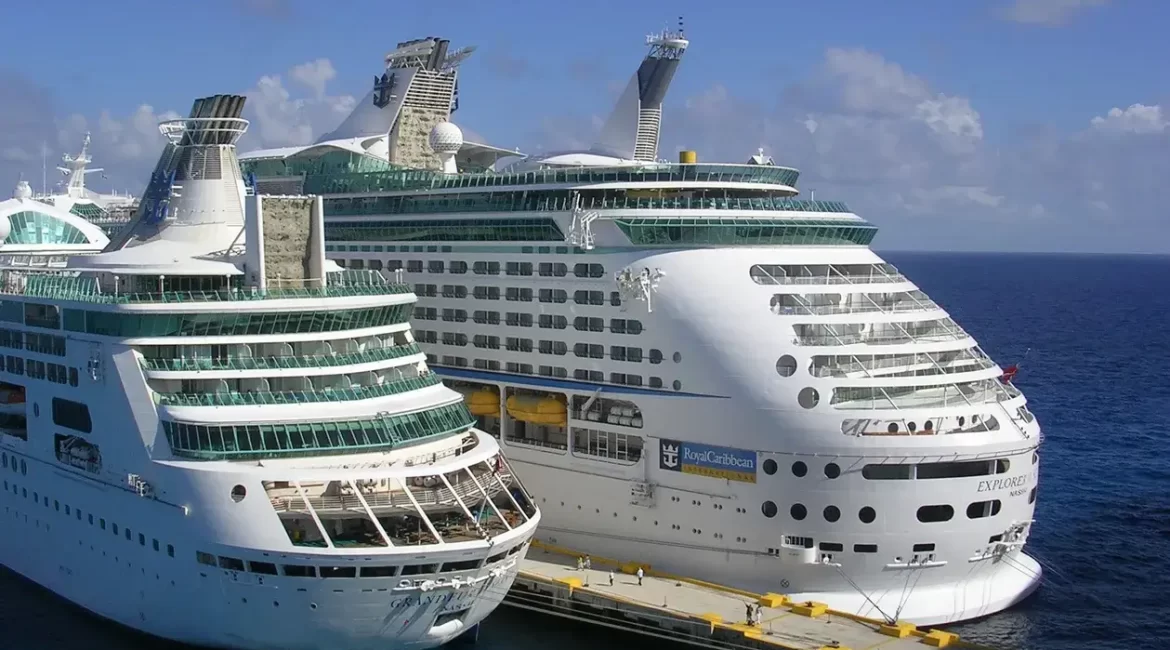 Two large cruise ships, the Explorer of the Seas and Grandeur of the Seas, docked side-by-side in a calm ocean